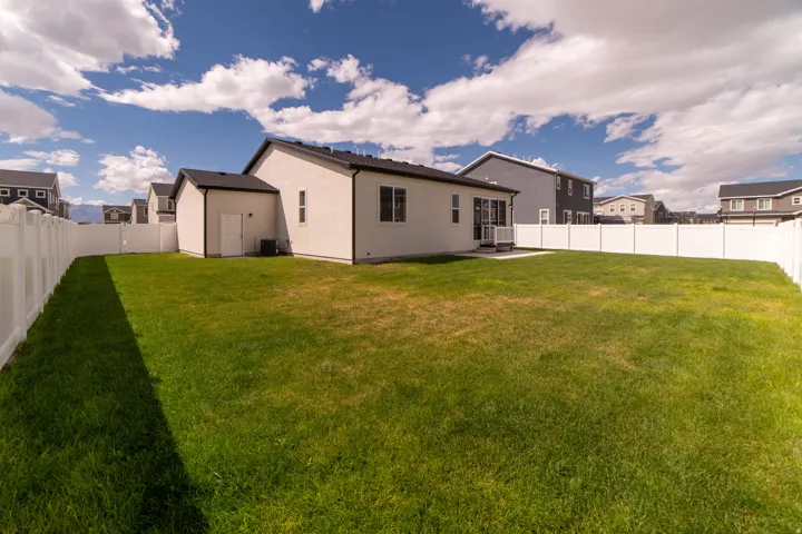 Expansive backyard with a manicured lawn, full vinyl privacy fencing, and a white exterior home with black-framed windows
