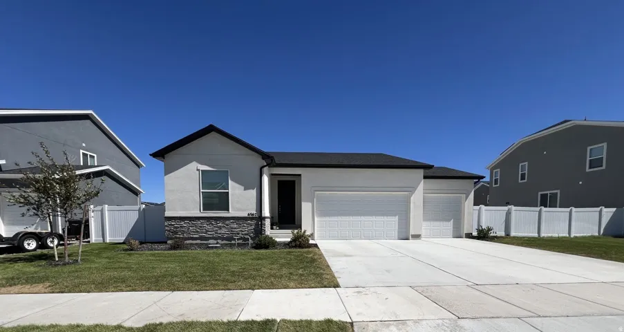 Contemporary single-story residence with a two-car garage, dark asphalt shingle roof, and light stucco exterior with stone veneer accents