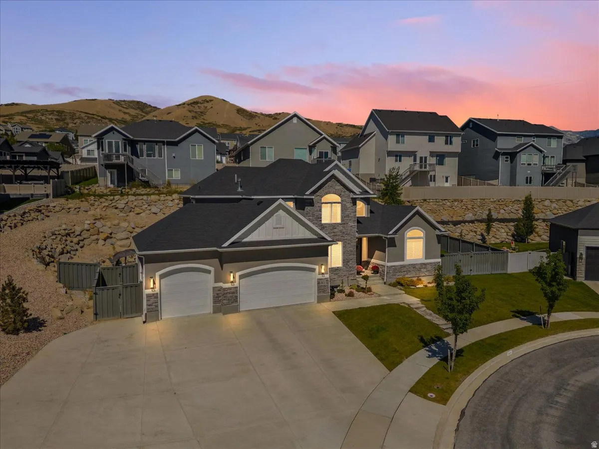 Contemporary residence featuring a three-car garage, stone and siding exterior, arched windows, and a landscaped front yard