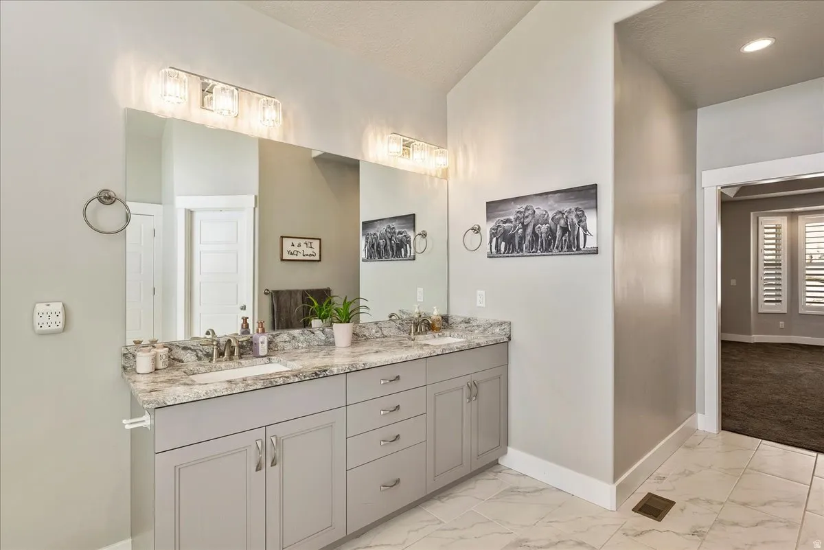 Dual vanity with stone-finish countertop, light gray cabinetry, and tile flooring