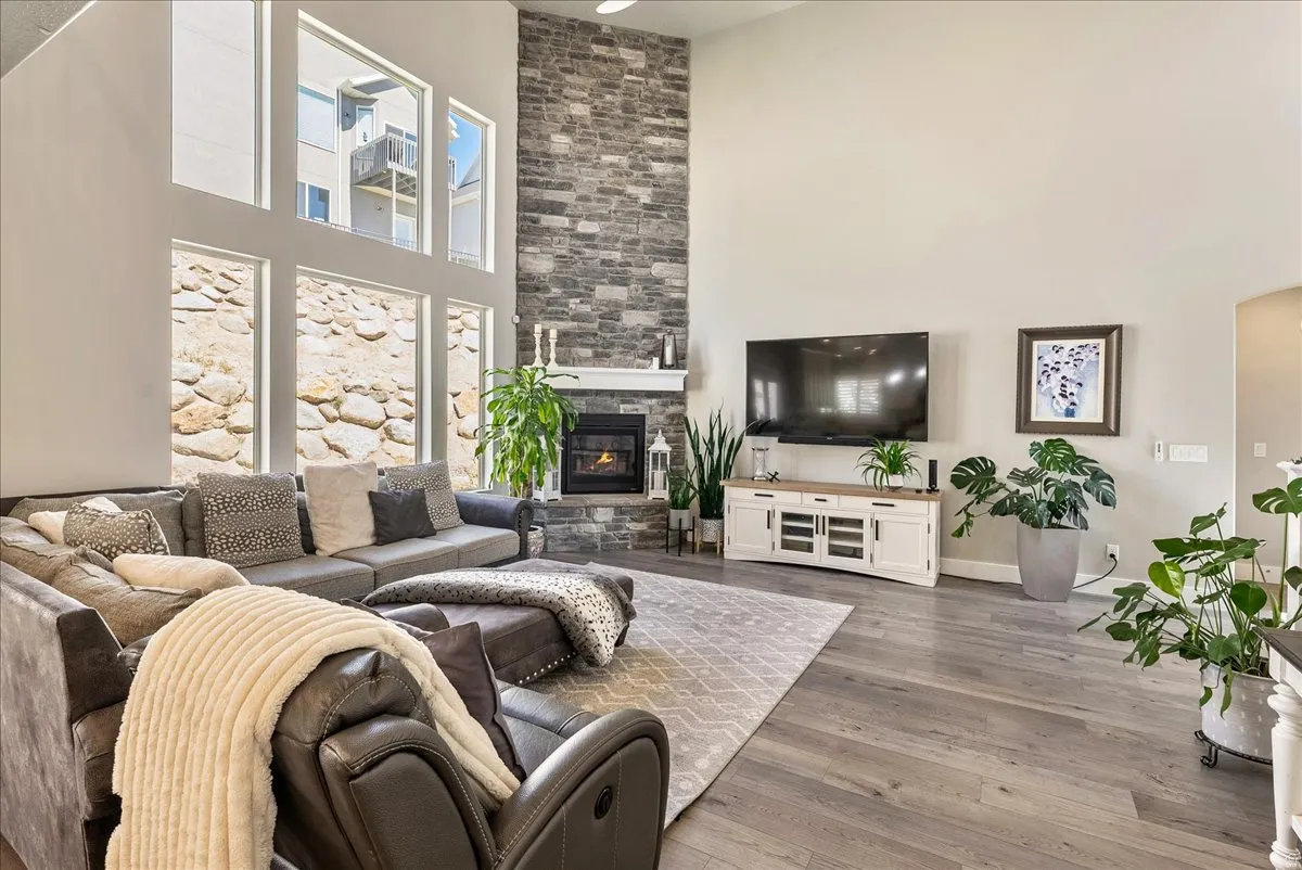 Two-story living area featuring a stone fireplace, wood-finish flooring, and expansive windows
