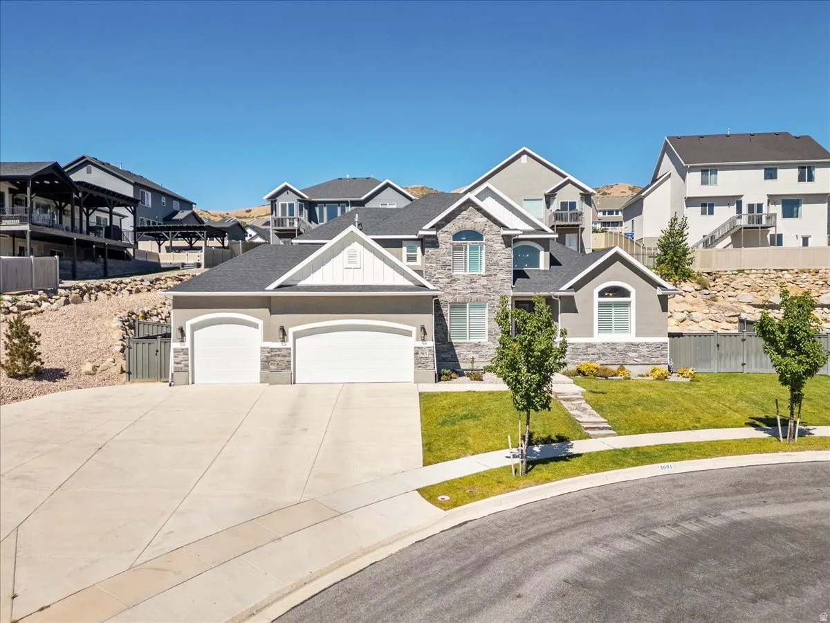 Three-car garage with arched doors, gray stucco and stone exterior, white trim accents, arched window, and concrete driveway