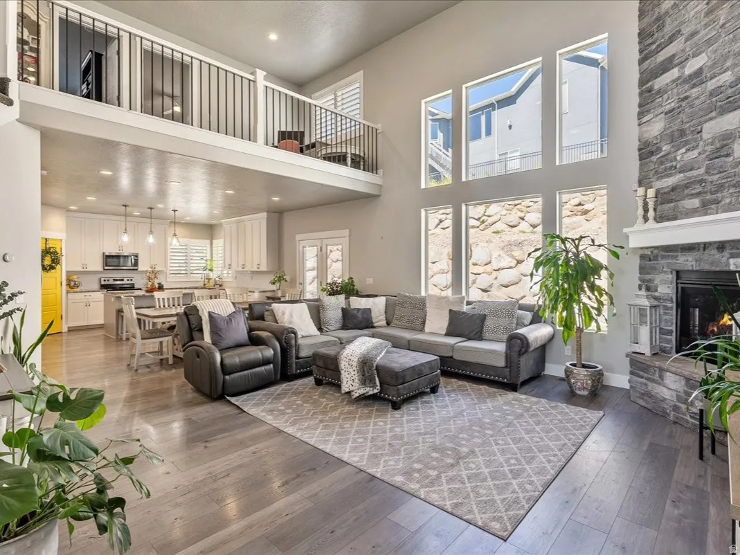 Two-story great room with a stone fireplace, wood-finish flooring, and a second-story interior balcony