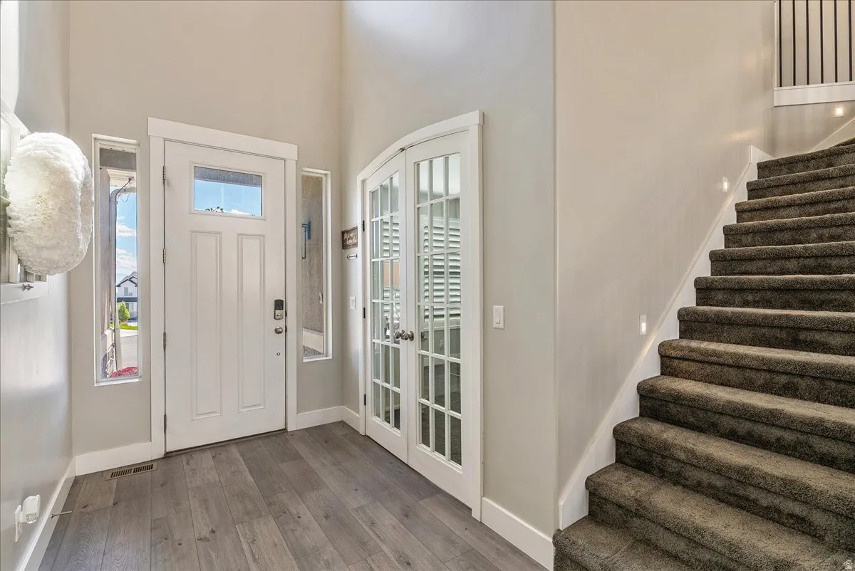 Two-story entry featuring wood-finish flooring, a white front door with transom and sidelights, and French doors