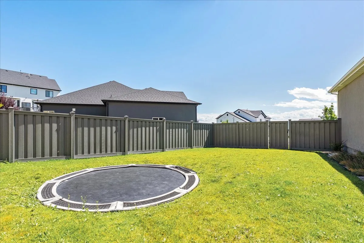 Expansive backyard featuring a manicured lawn, full perimeter fencing, and an in-ground trampoline