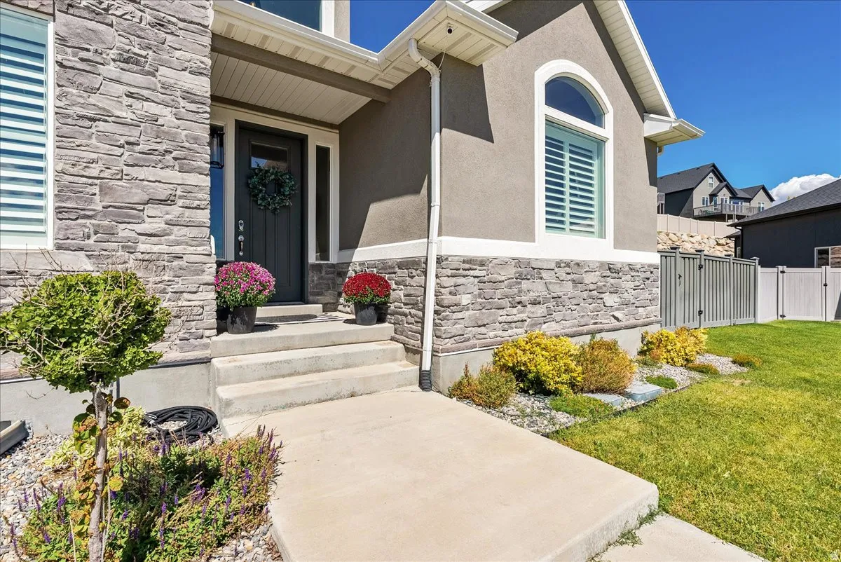 Stone veneer facade, stucco exterior, arched window, concrete walkway, and landscaped garden beds