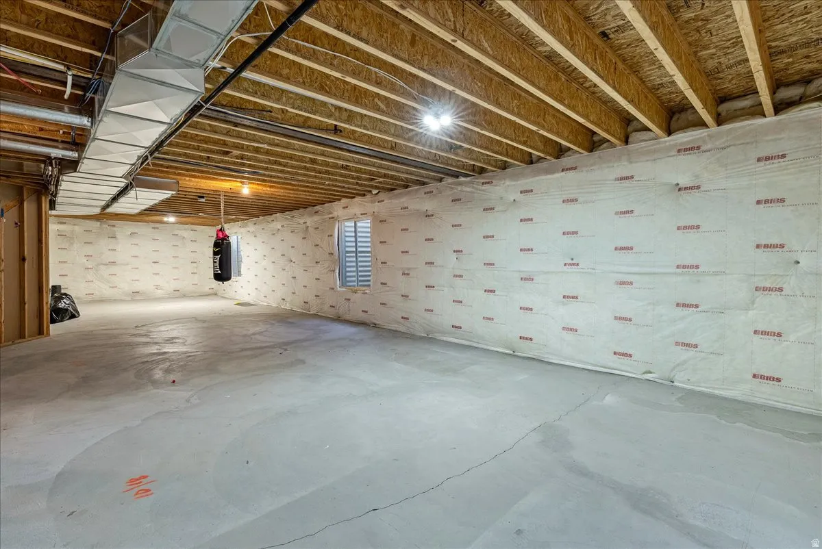 Expansive unfinished basement level with exposed ceiling joists, concrete flooring, and an egress window