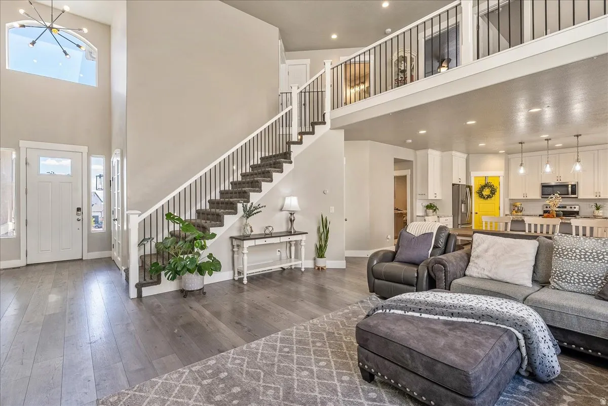 Vaulted entry with an arched window and chandelier, wood-finish flooring, and a grand staircase with wrought iron balusters