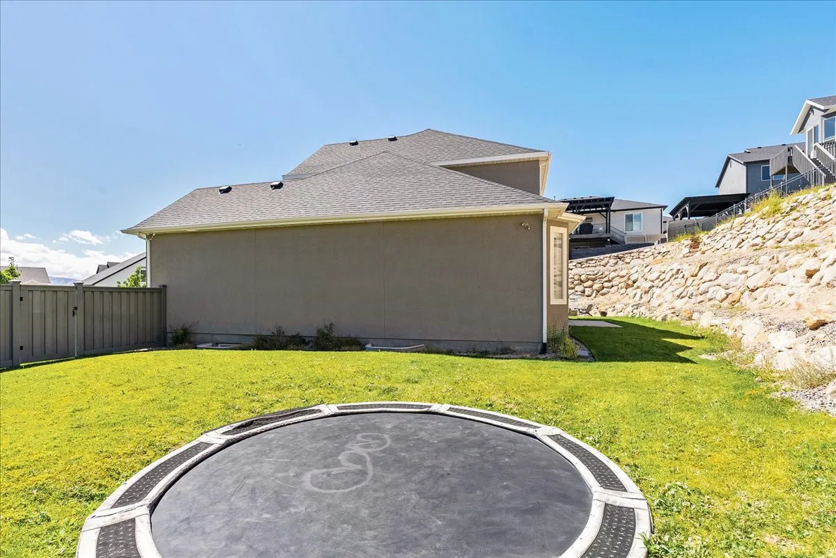Expansive green lawn, stucco exterior, sloped rock retaining wall, privacy fencing, and rear-facing windows