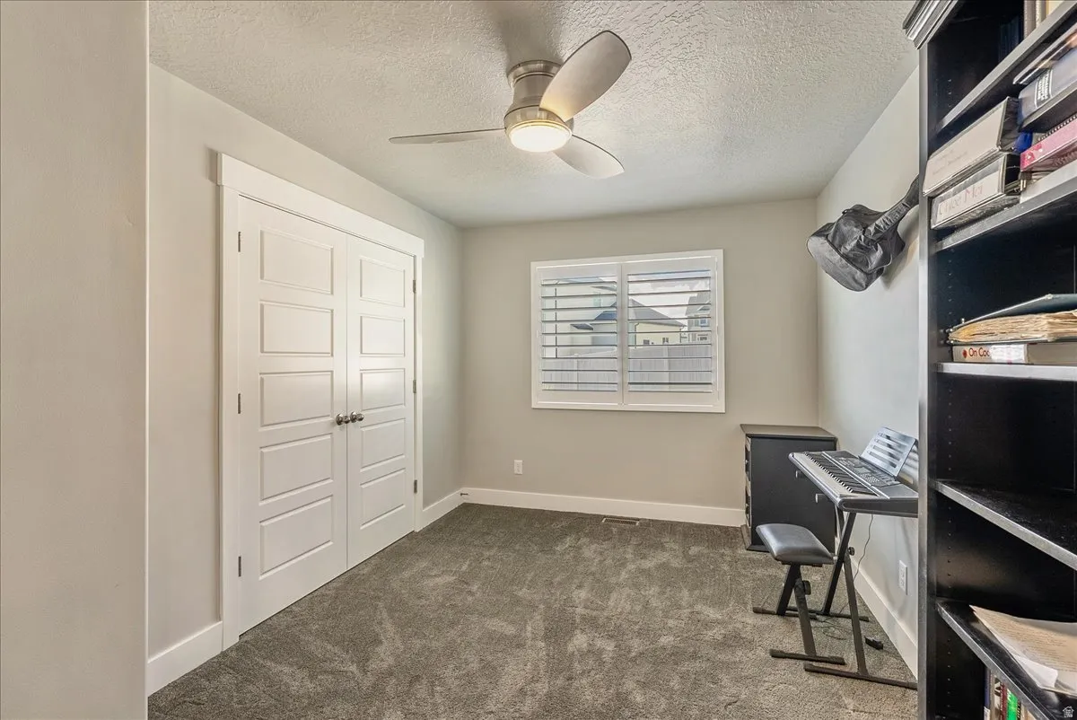 Carpeted bedroom with a ceiling fan, window with white louvered shutters