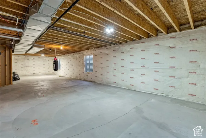 Expansive unfinished basement level with exposed ceiling joists, concrete flooring, and an egress window