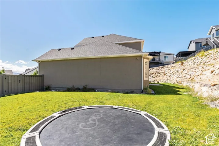 Expansive green lawn, stucco exterior, sloped rock retaining wall, privacy fencing, and rear-facing windows