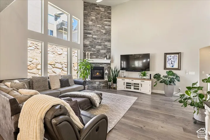 Two-story living area featuring a stone fireplace, wood-finish flooring, and expansive windows