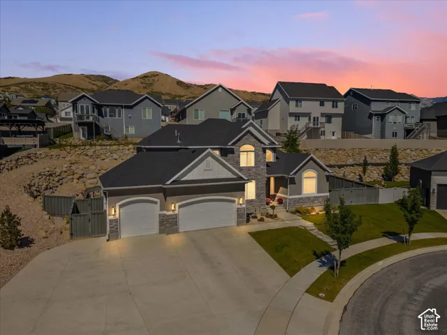 Contemporary residence featuring a three-car garage, stone and siding exterior, arched windows, and a landscaped front yard