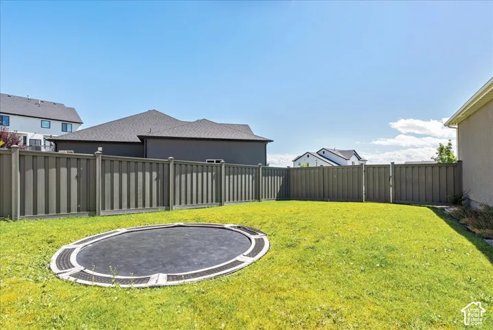 Expansive backyard featuring a manicured lawn, full perimeter fencing, and an in-ground trampoline