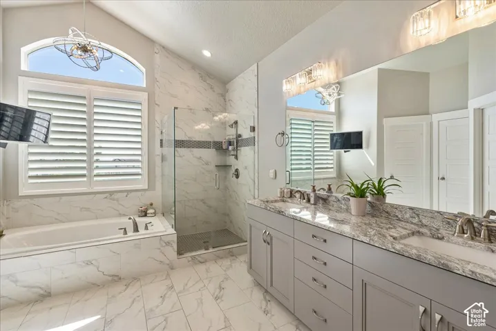 Primary Bathroom- Vaulted ceiling with an arched window, plantation shutters, a glass-enclosed shower, a built-in tub, and a dual vanity with a stone countertop