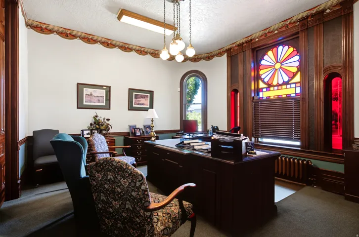 Stained glass window detail, arched window, wood wall paneling, ceiling-mounted lighting, and a radiator