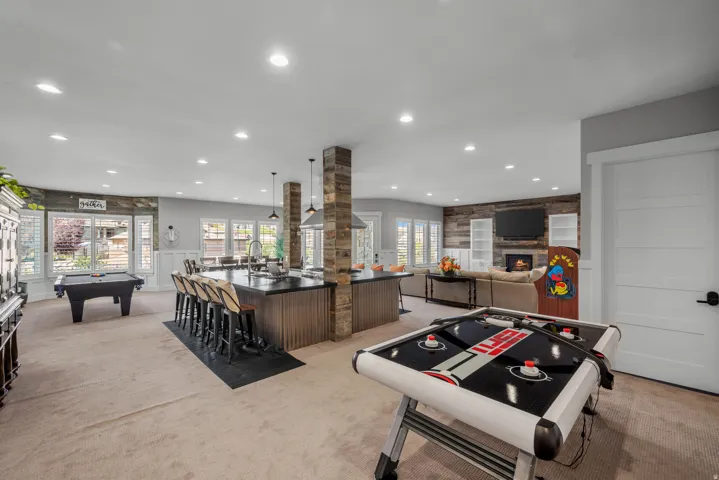 Open-concept living space featuring recessed lighting, a stone-clad fireplace with built-in shelving, an expansive island with seating, and wood-finish accent walls