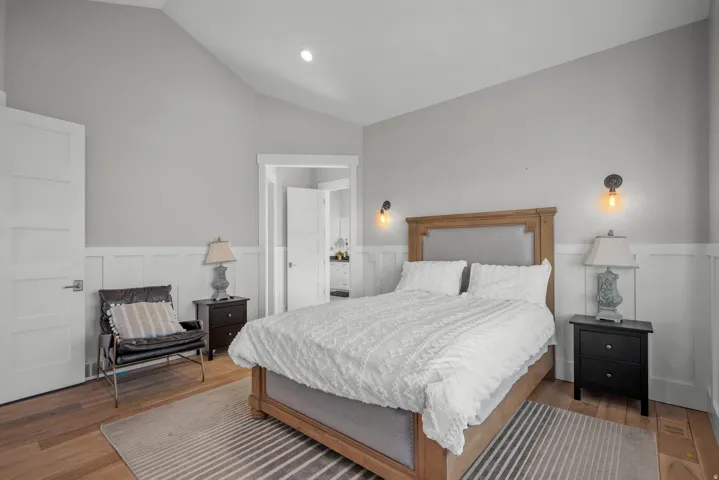 Wood-finish flooring, accent wall with wainscoting, recessed lighting, vaulted ceiling, and white paneled doors