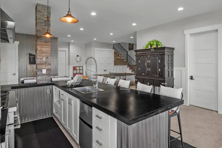 Kitchen island with dark countertop, stainless steel sink, and integrated dishwasher
