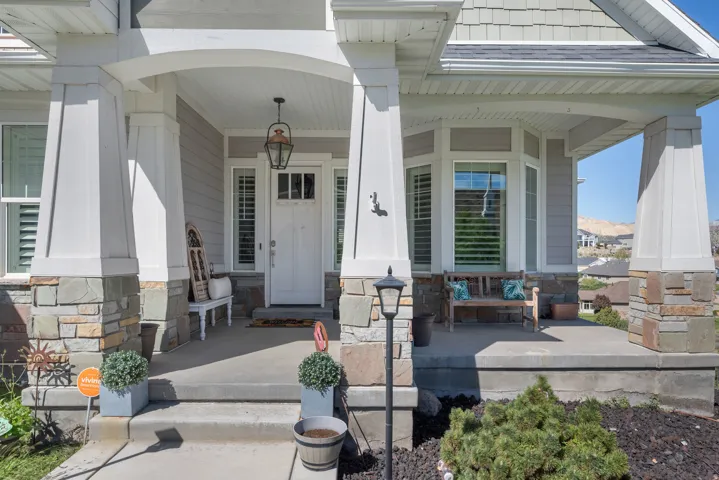 Covered front porch with stone and column accents, a paneled entry door, and a bay window featuring louvered shutters