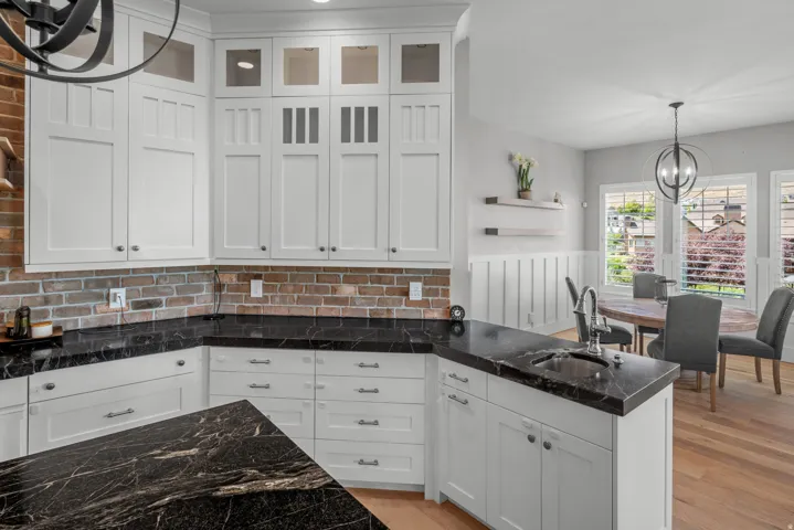 White shaker cabinetry with glass-front accents, dark veined countertops, and brick-patterned backsplash