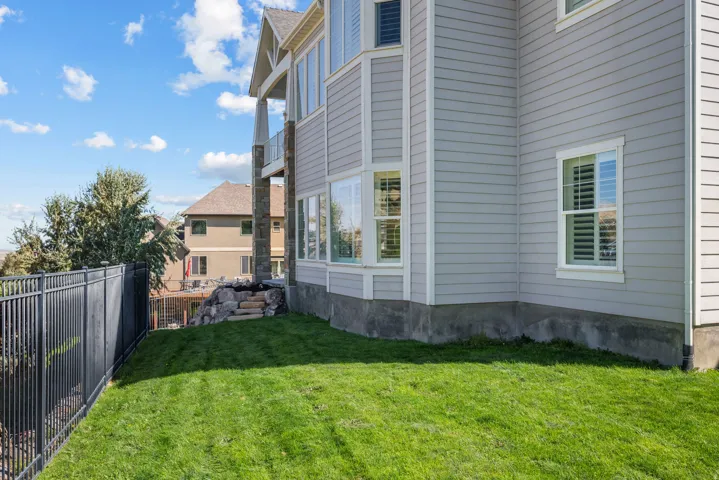 Expansive grassy side yard with a black metal fence, rock retaining wall, and stone steps