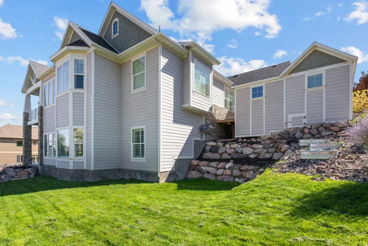 Light gray horizontal siding with white trim, bay window, stone retaining wall, and green lawn