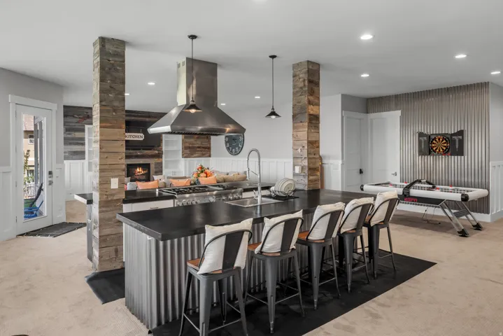 Expansive island with dark countertop and seating, stainless steel range hood, stone-clad structural elements, shiplap accent wall, and corrugated metal wall paneling