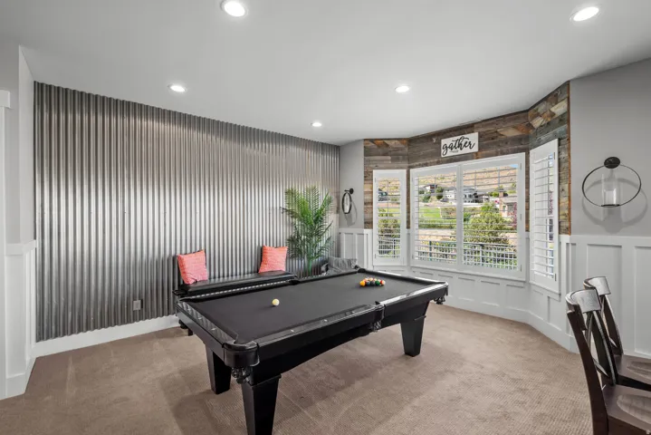 Recessed lighting illuminates the room, featuring a corrugated metal accent wall and a bay window with plantation shutters