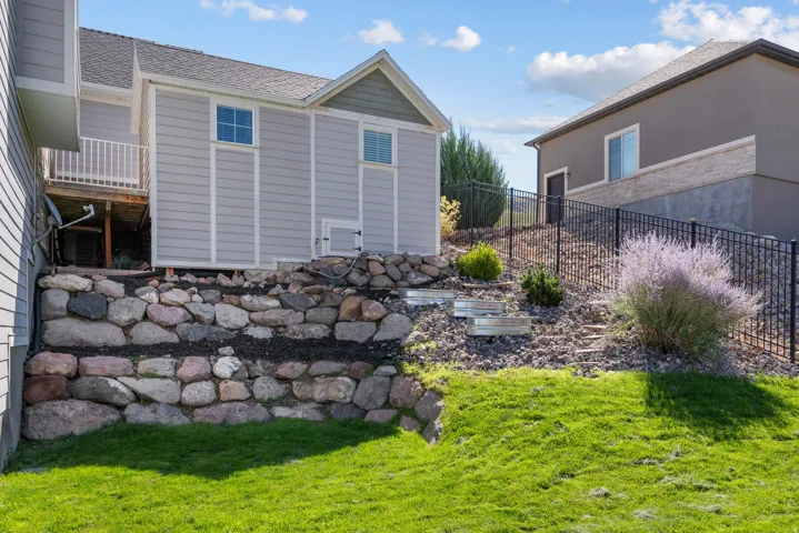 Manicured lawn with a stone retaining wall and an adjacent landscaped hillside featuring planted shrubs and a black metal fence