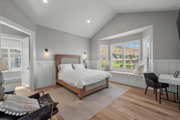 Vaulted ceiling with recessed lighting, wood-finish flooring, bay window with integrated bench seating, white plantation shutters, and board and batten wall detailing
