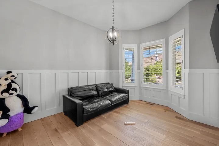 Wood-finish flooring, wainscoting, three windows with plantation shutters, and a spherical chandelier