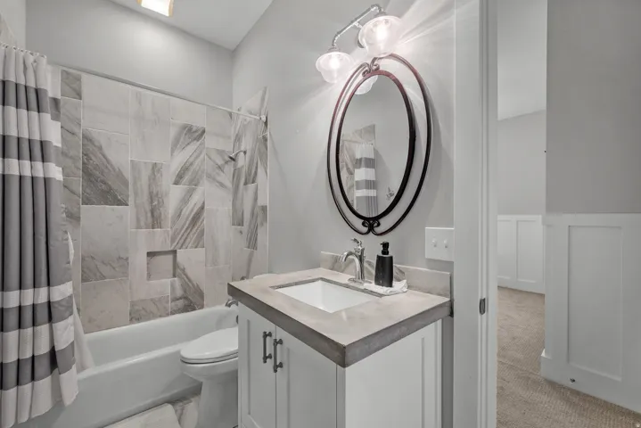 Bathroom featuring a white vanity with dark hardware, a gray countertop, an oval framed mirror, and a tile tub surround with an integrated niche