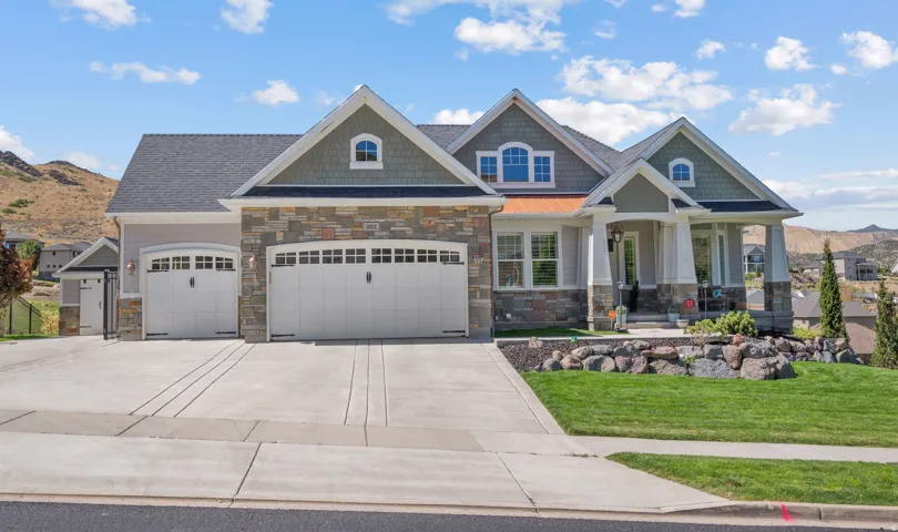 Stone and siding exterior with a multi-car driveway, arched garage doors, a covered front entry, and a manicured lawn