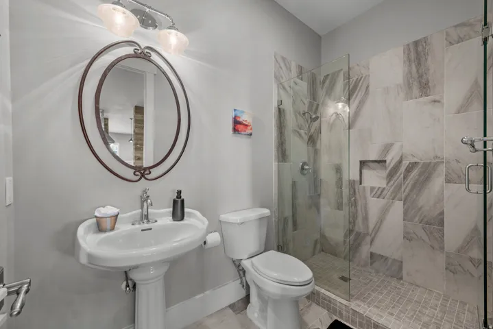 Pedestal sink with an oval mirror, glass-enclosed shower, and tiled shower walls with a built-in niche