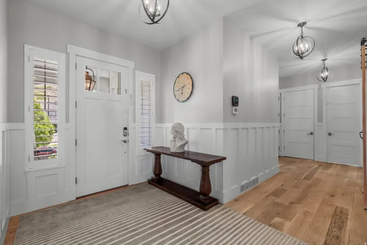 Entryway featuring wood-finish flooring, wainscoting, a paneled front door with sidelights, and overhead lighting