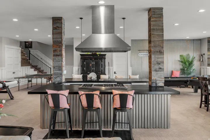 Central island with a built-in cooktop and stainless steel range hood, stone-clad structural columns, and wainscoting