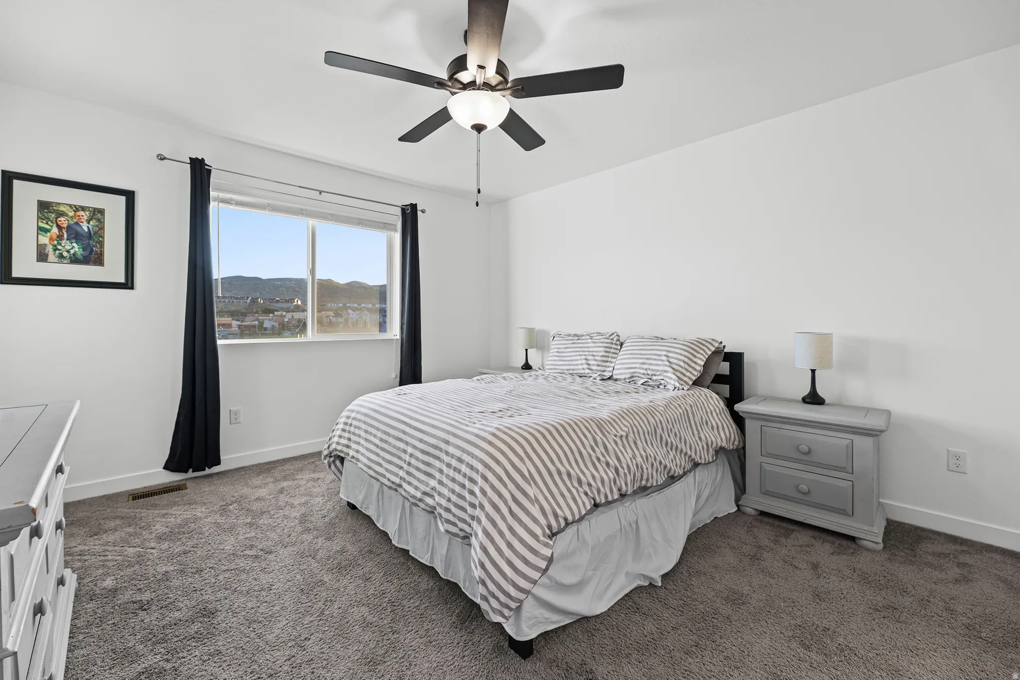 Window with mountain scenery, ceiling fan with integrated lighting, clean white walls, and gray carpet flooring