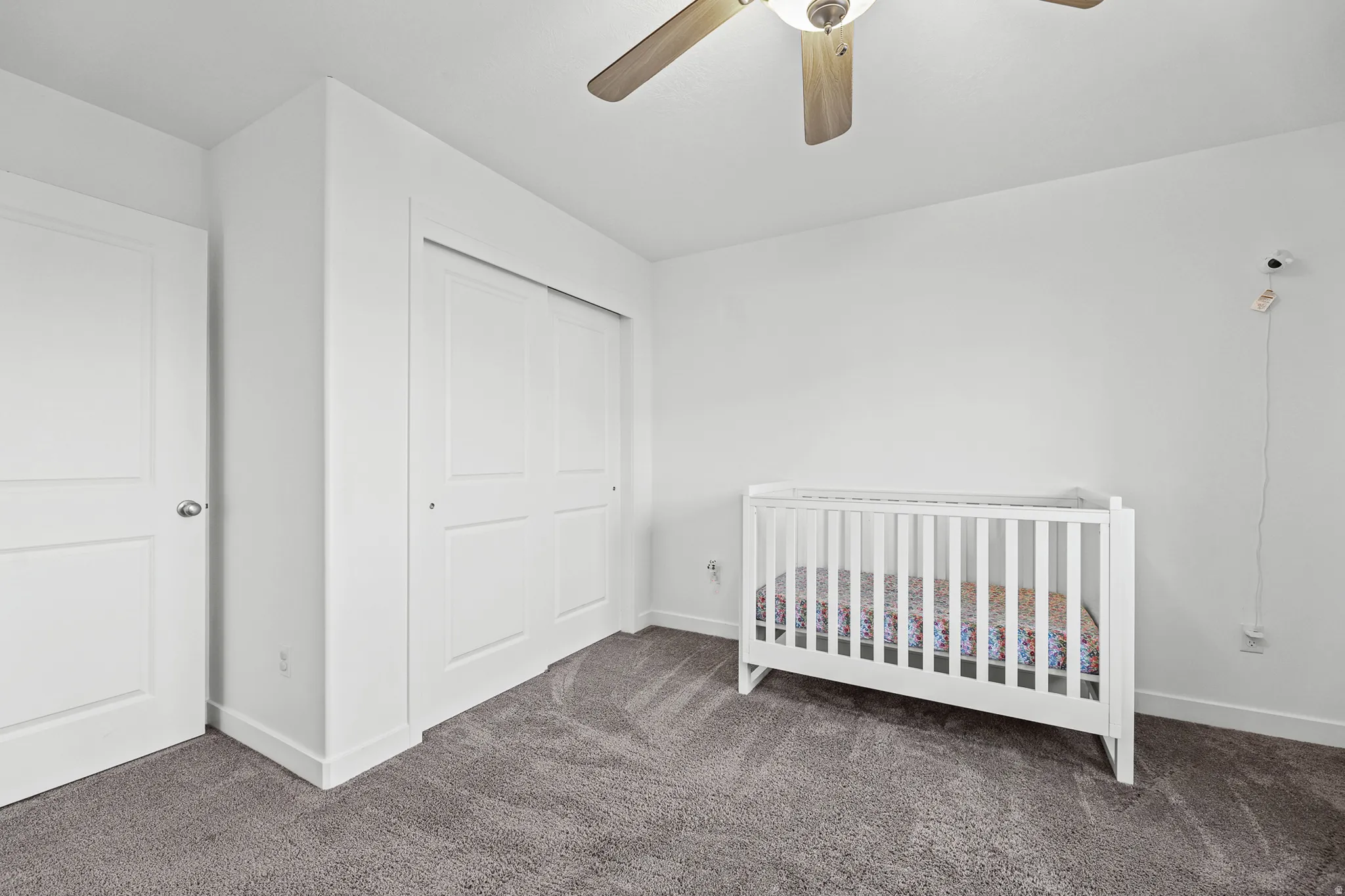 White walls, gray carpet flooring, and a ceiling fan with wood-tone blades
