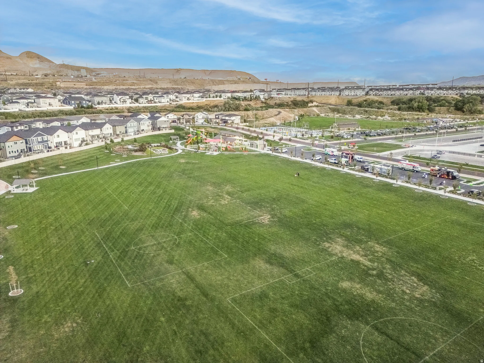 Expansive green space featuring marked sports fields, a playground area, and a white gazebo