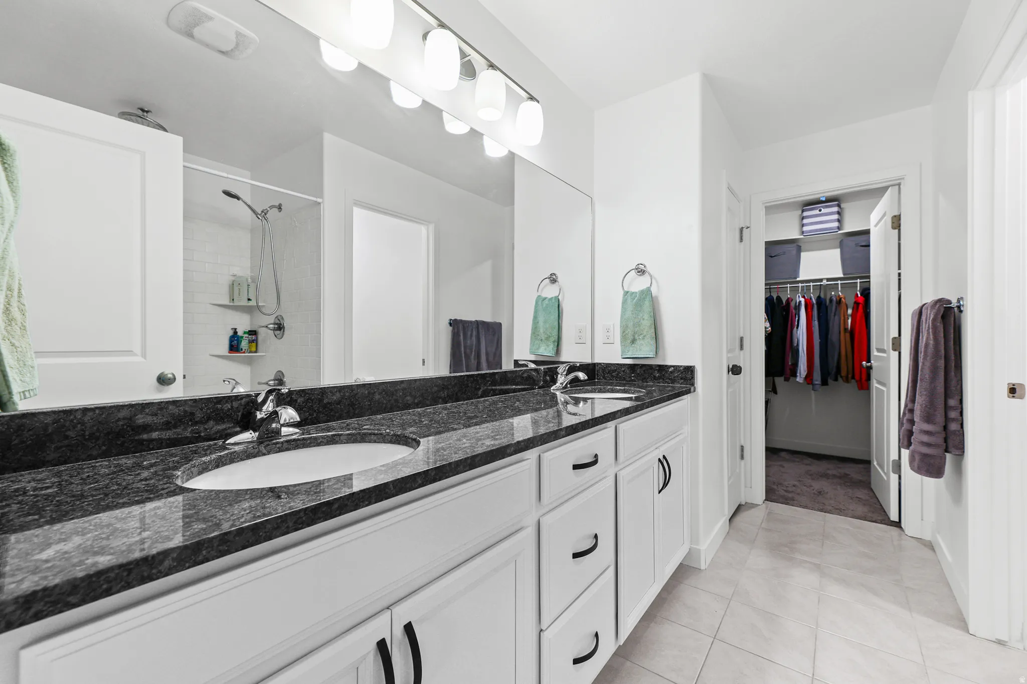 Double vanity with undermount sinks, dark stone countertop, white cabinetry, and polished chrome fixtures