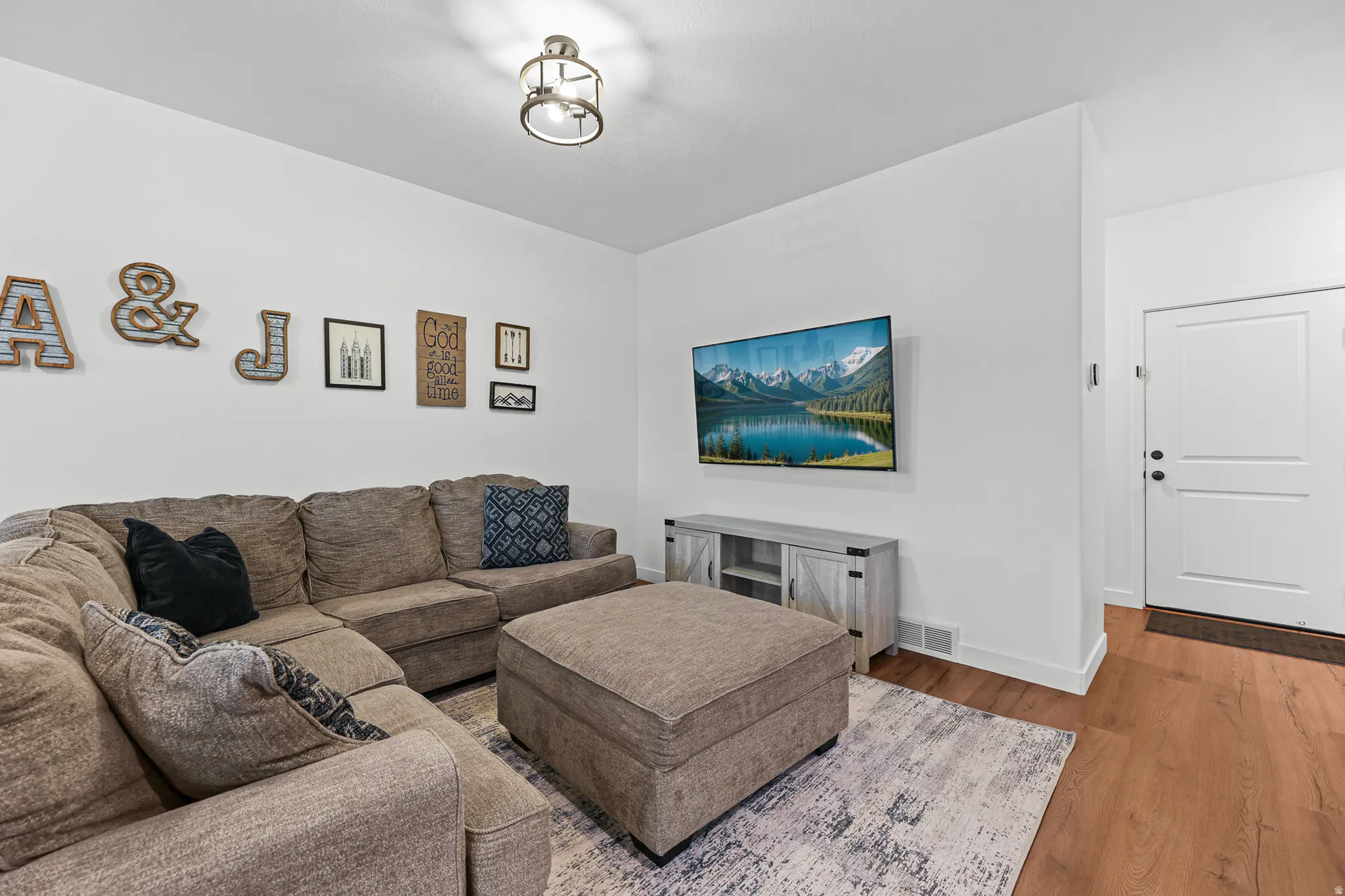 Wood-finish flooring, white walls, white two-panel door with black hardware, and a ceiling-mounted light fixture