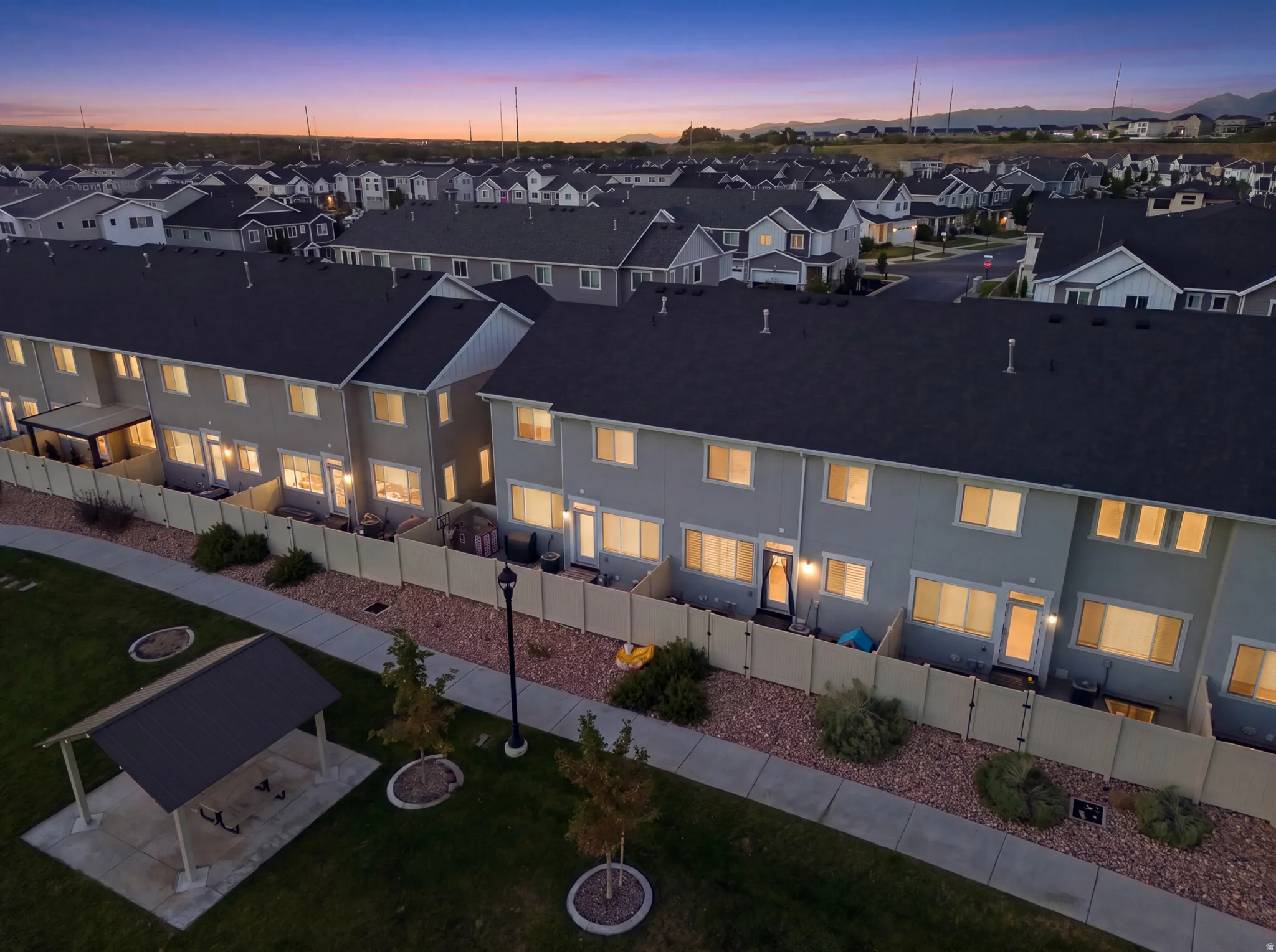 Townhome exteriors with dark roofing, individual fenced patios, and a community green space with a covered picnic area