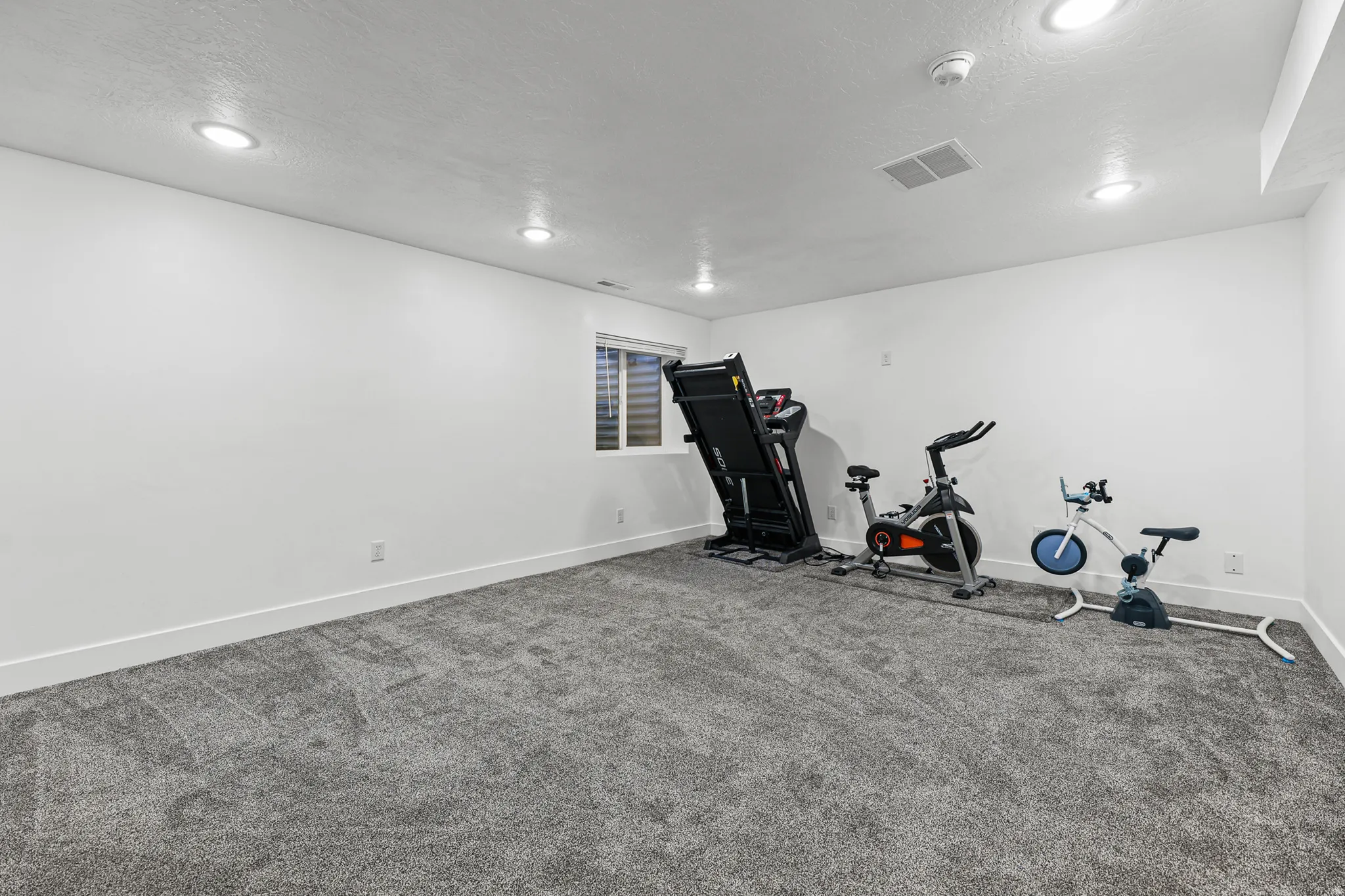 White walls, recessed lighting, and a single window with blinds