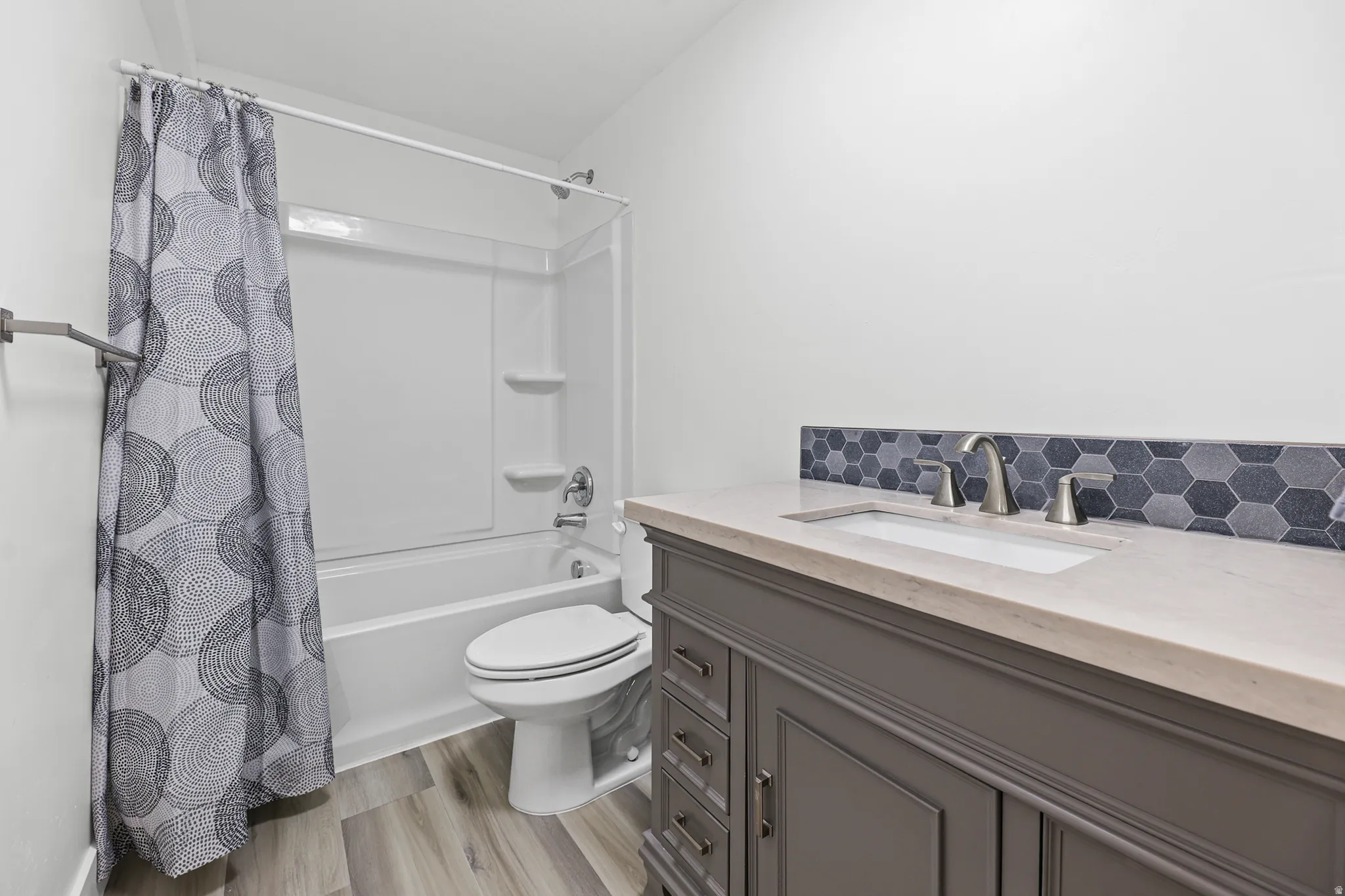 Vanity with an integrated rectangular sink, light-toned countertop, and hexagonal tile backsplash