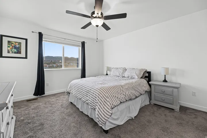 Window with mountain scenery, ceiling fan with integrated lighting, clean white walls, and gray carpet flooring