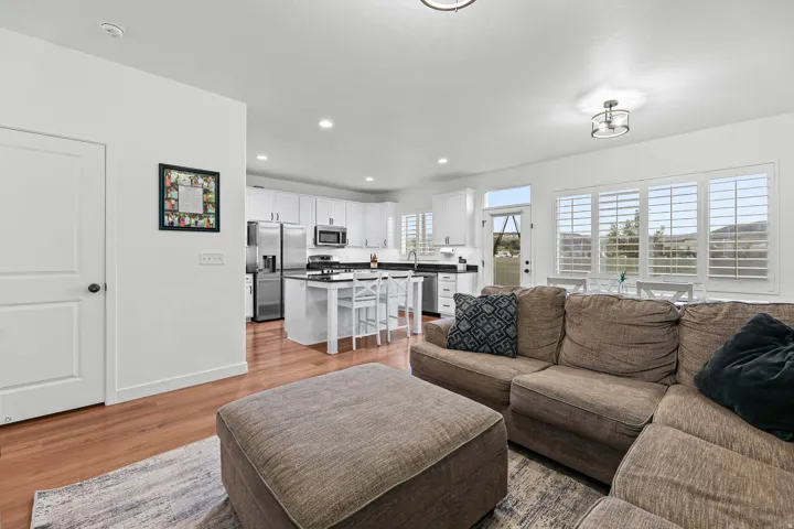 Open-concept living space featuring wood-finish flooring, white kitchen cabinetry, stainless steel appliances, a kitchen island with seating, and plantation shutters