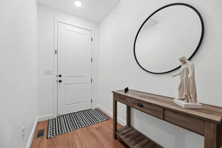 White paneled door with black hardware, wood-finish flooring, recessed ceiling light, and a console table with a lower shelf