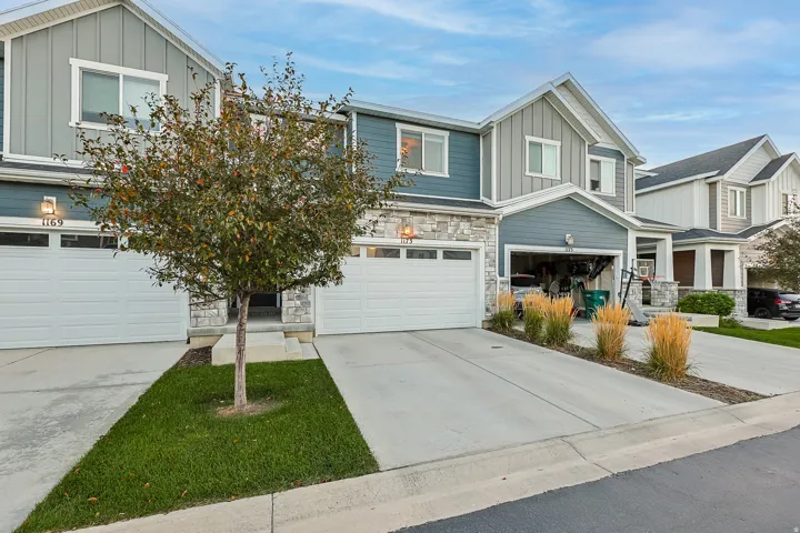 Two-story multi-unit exterior featuring vertical siding, stone accents, attached garages, and a concrete driveway